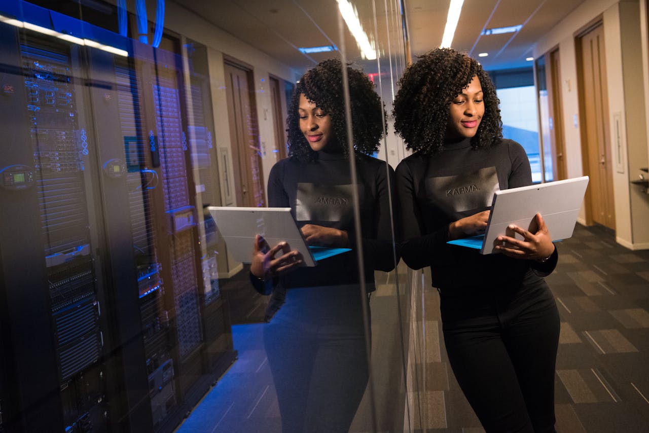 our-story African American woman standing in modern office using laptop, reflecting professionalism and technology engagement.