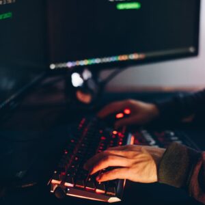 From above of crop anonymous cyber spy typing on computer keyboard with data on screen at night