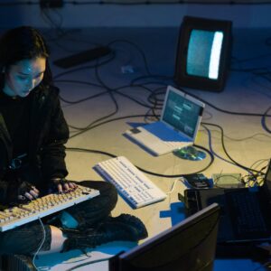 Young Asian woman engaged in computer hacking in a dimly lit, technologically equipped room.